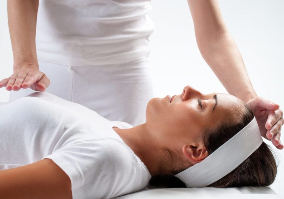 Close up of chiropractor’s hands doing reiki on young woman.One hand on head and one hand on chest.