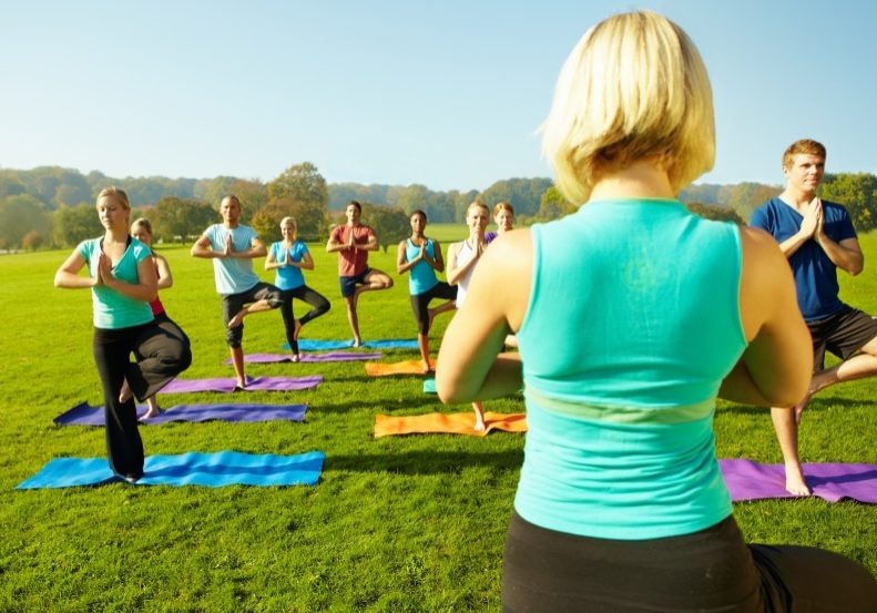 Rear view of a yoga instructor as she faces her class while outdoors